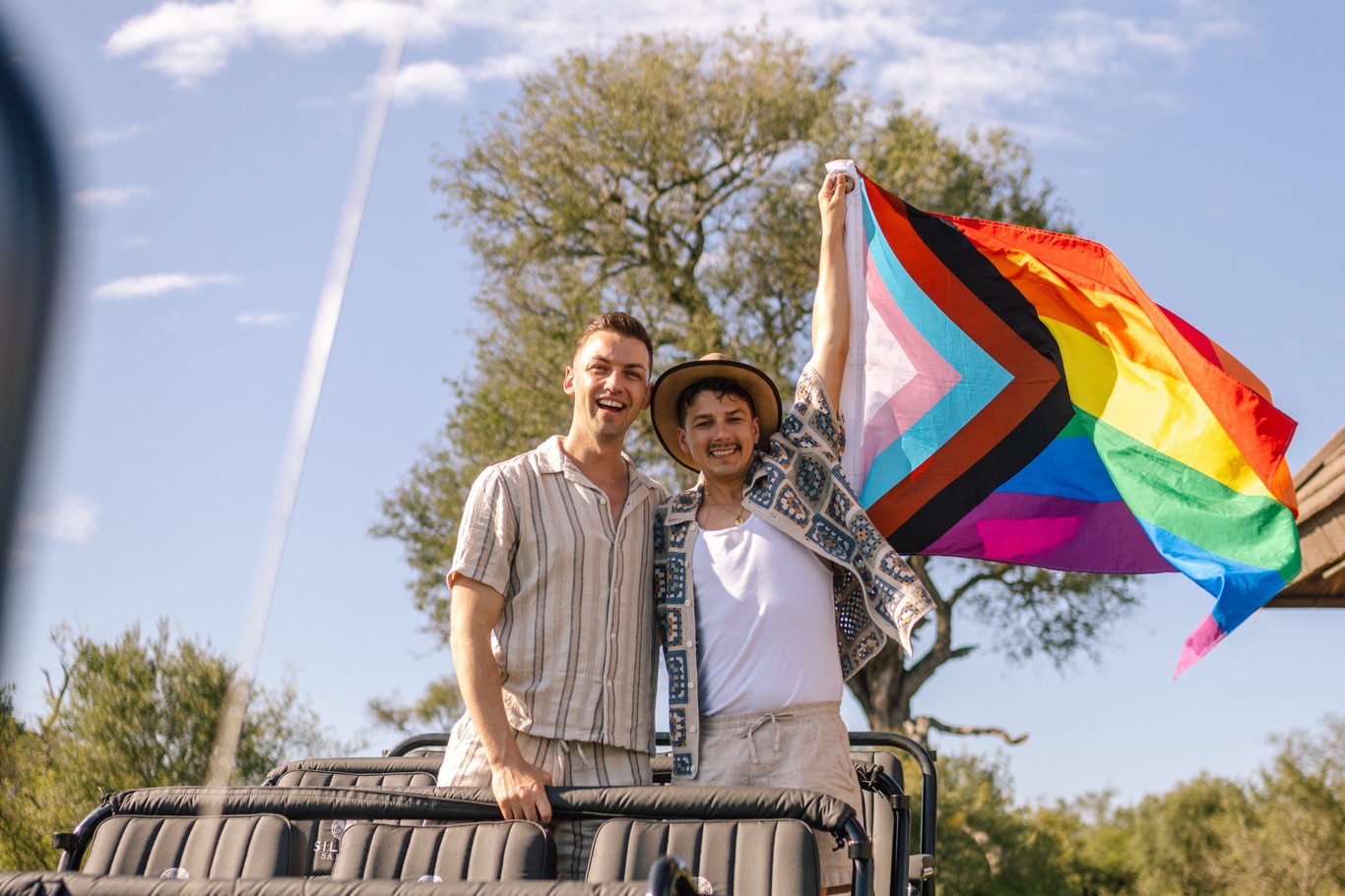 Michael and Matt holding a rainbow flag on a game drive vehicle at Silvan Safari